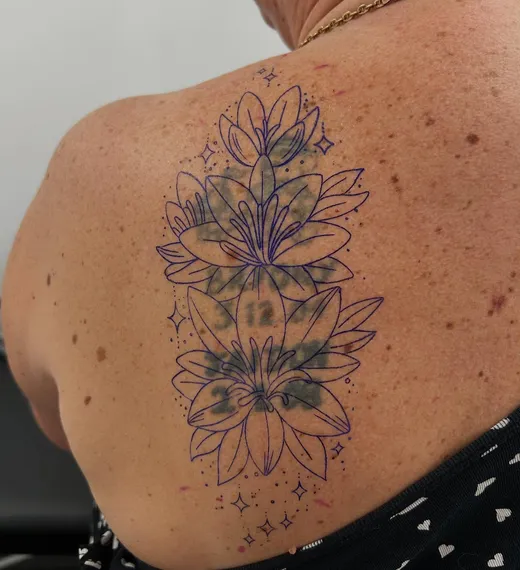 A stencil of lilies placed over an old tattoo on a client’s back, before tattooing
