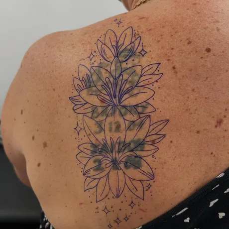 Stencil stage: Lilies over an old back piece, with the old tattoo visible underneath